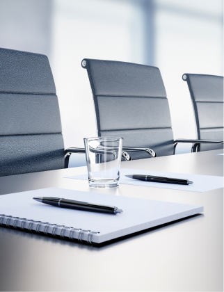 A table with notebooks and glasses of water. There are three office chairs next to it.